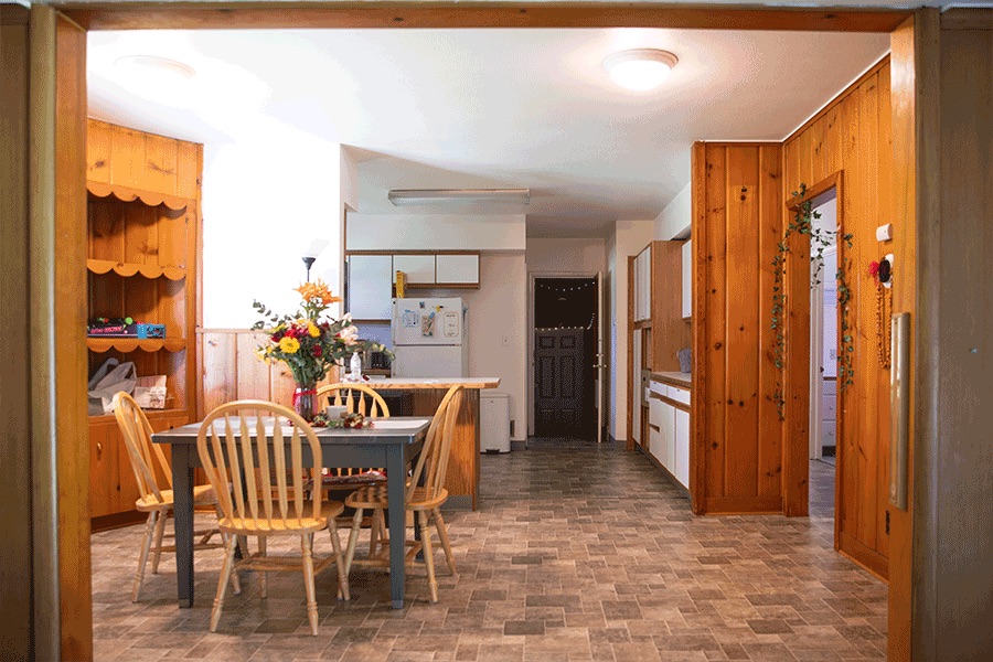 An open dining room with paneled walls and cabinetry, a table with four chairs, and a view into the kitchen.
